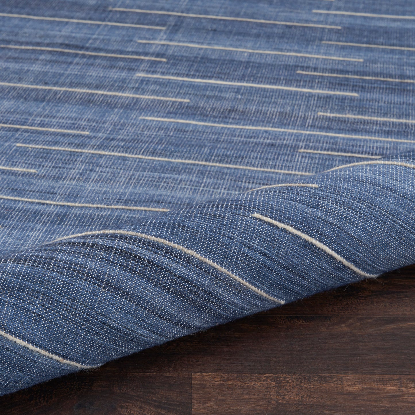 Blue denim-like rug with white stitch lines and a folded edge on a dark wood surface.