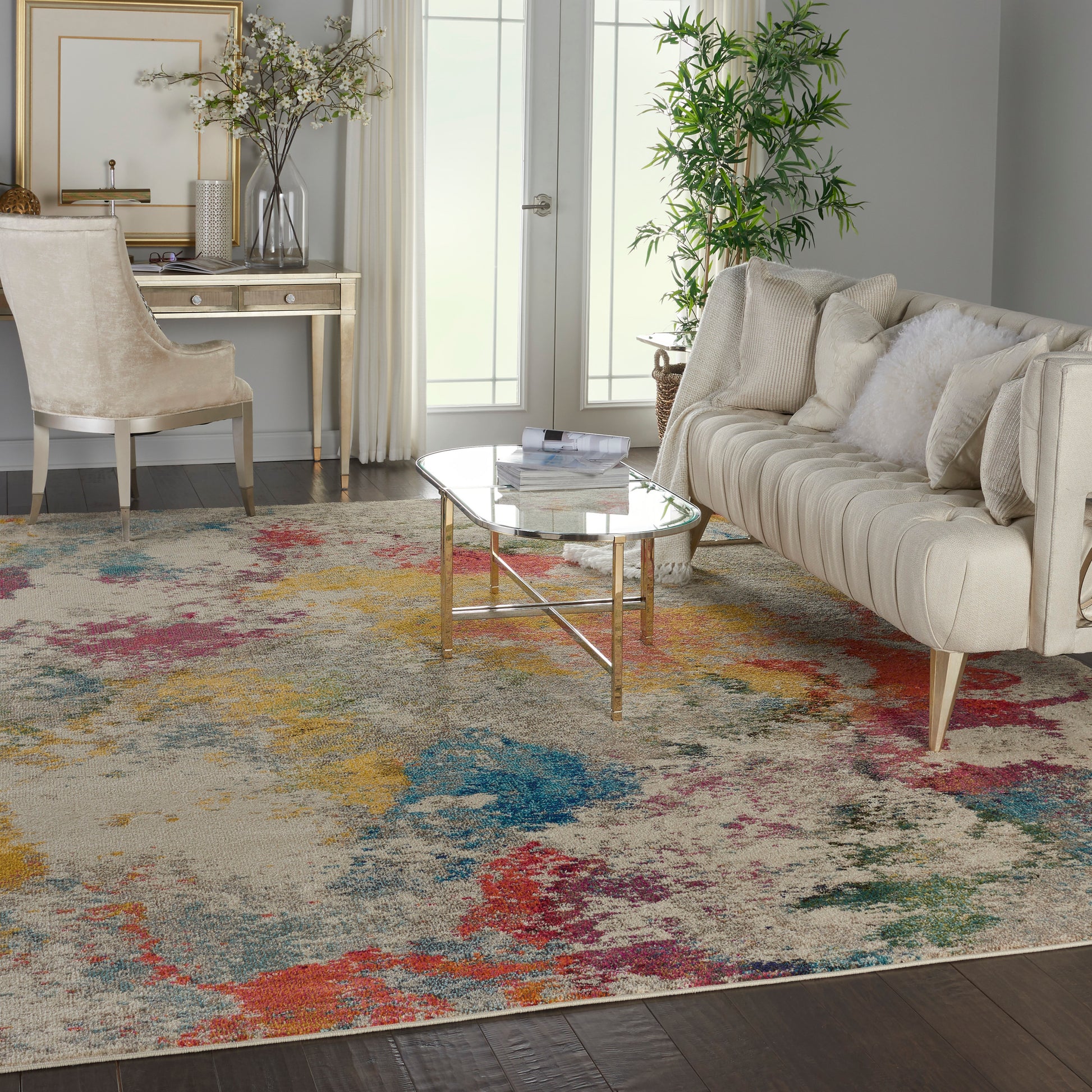 Living room with a beige sofa, glass-top coffee table on gold legs, and a vibrant abstract multicolor rug.