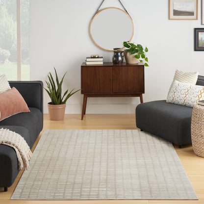 Beige woven area rug with a subtle grid pattern in a neutral living room with gray sofas and a mid-century wood sideboard.
