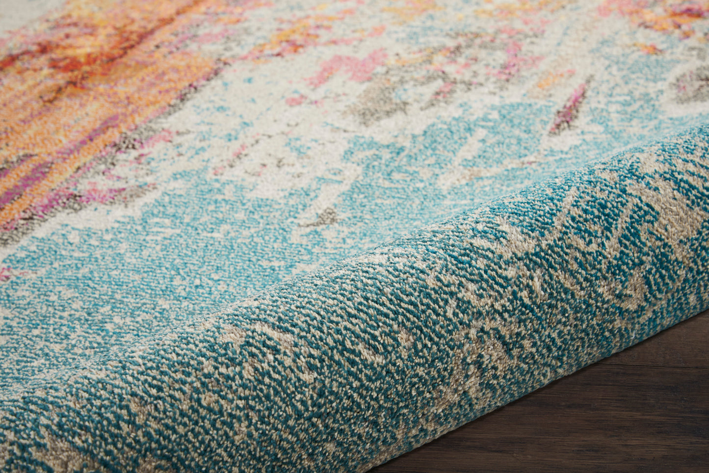 Close-up of a turquoise-bordered area rug with abstract pink, orange, cream pattern on dark wood floor.