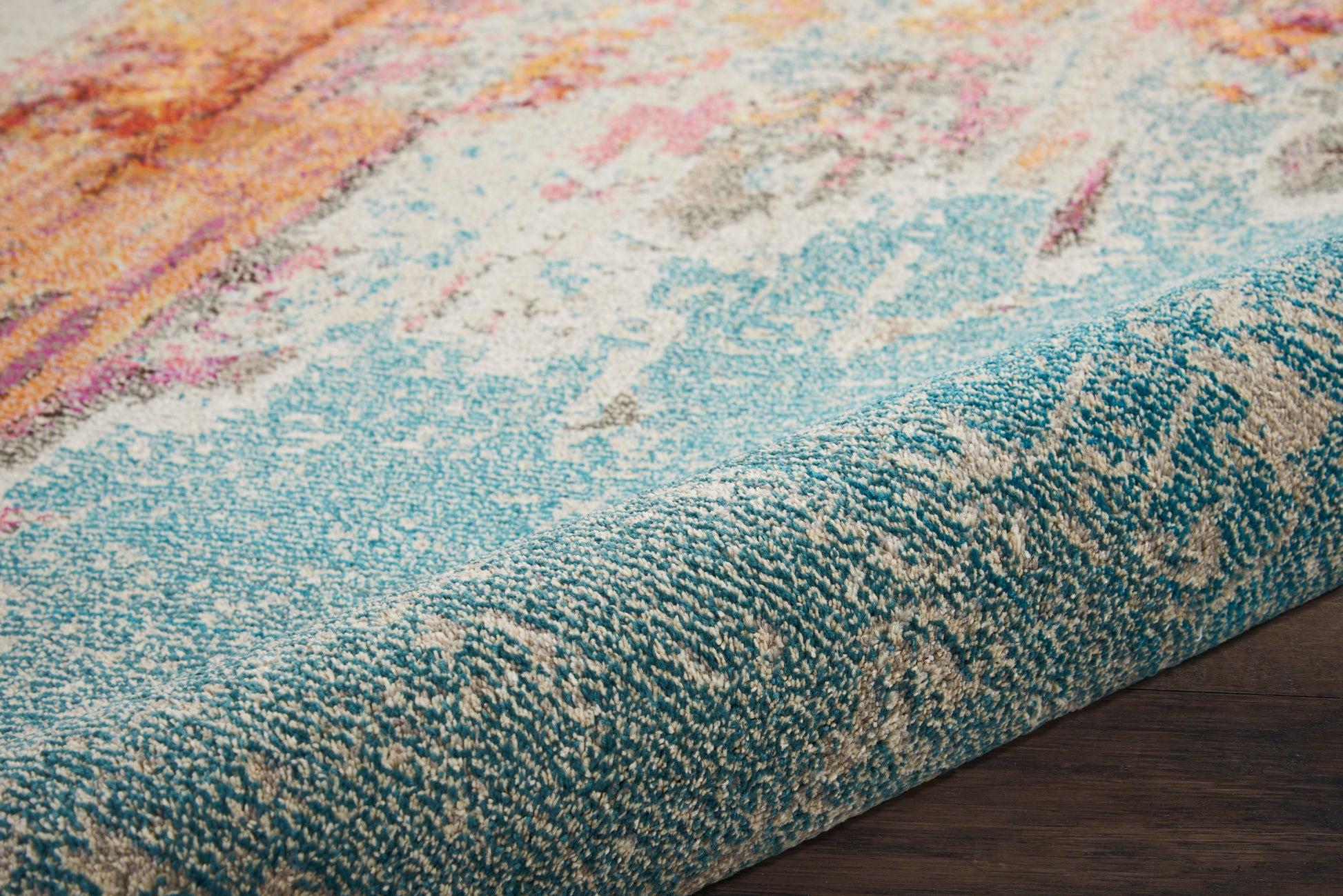 Close-up of a turquoise-bordered area rug with abstract pink, orange, cream pattern on dark wood floor.