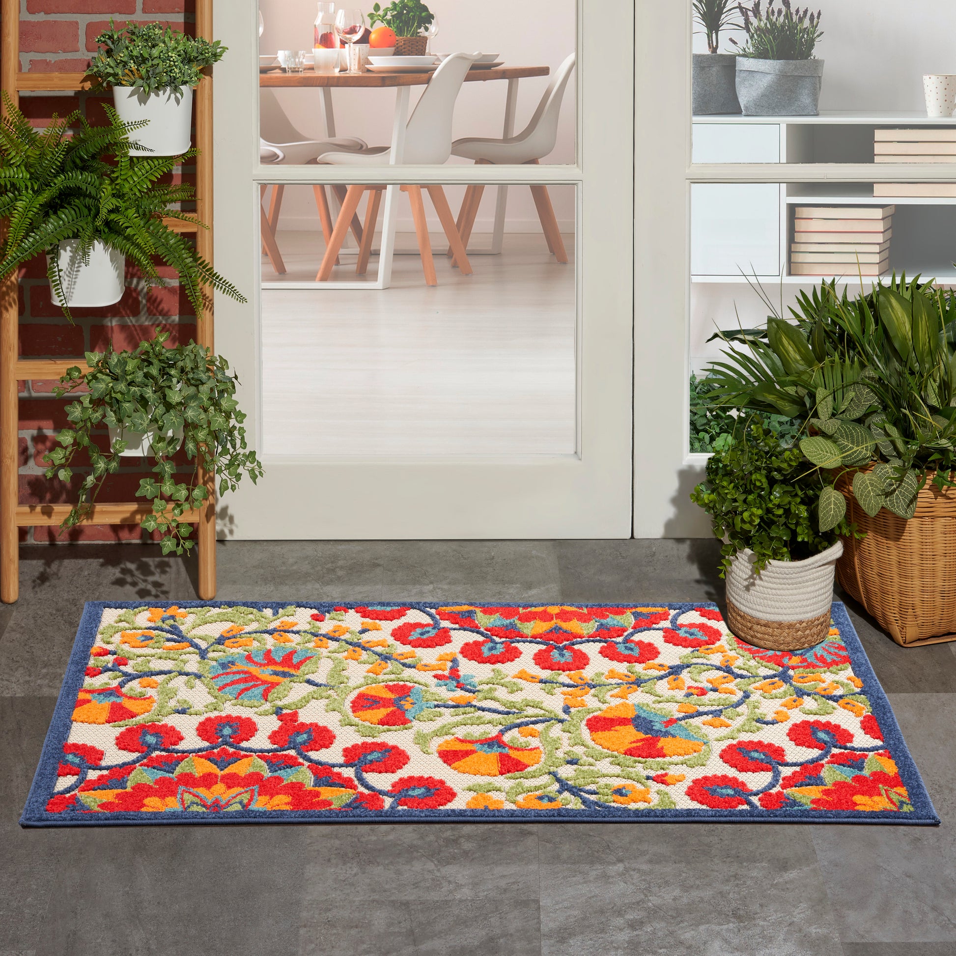Colorful floral outdoor doormat with blue border at doorway; multicolor red, yellow, green pattern.