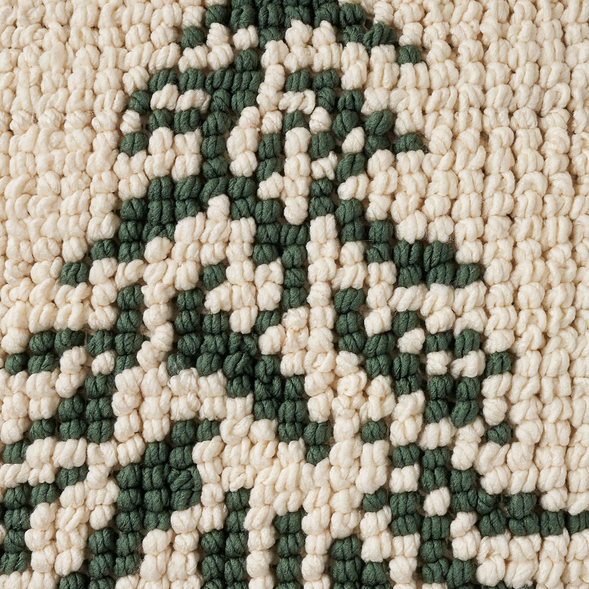 Close-up of a cream-beige chunky-loop rug with dark green geometric motif and textured weave