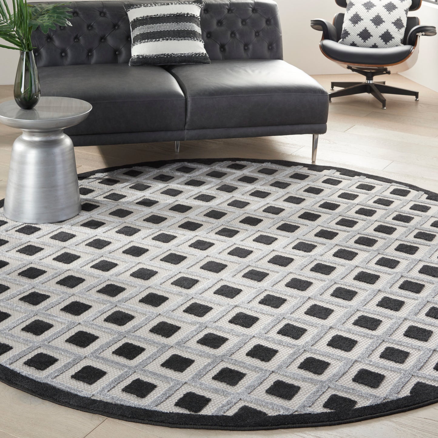 Round geometric area rug with grey background and black square grid in a modern living room with a dark tufted sofa.