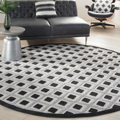 Round geometric area rug with grey background and black square grid in a modern living room with a dark tufted sofa.