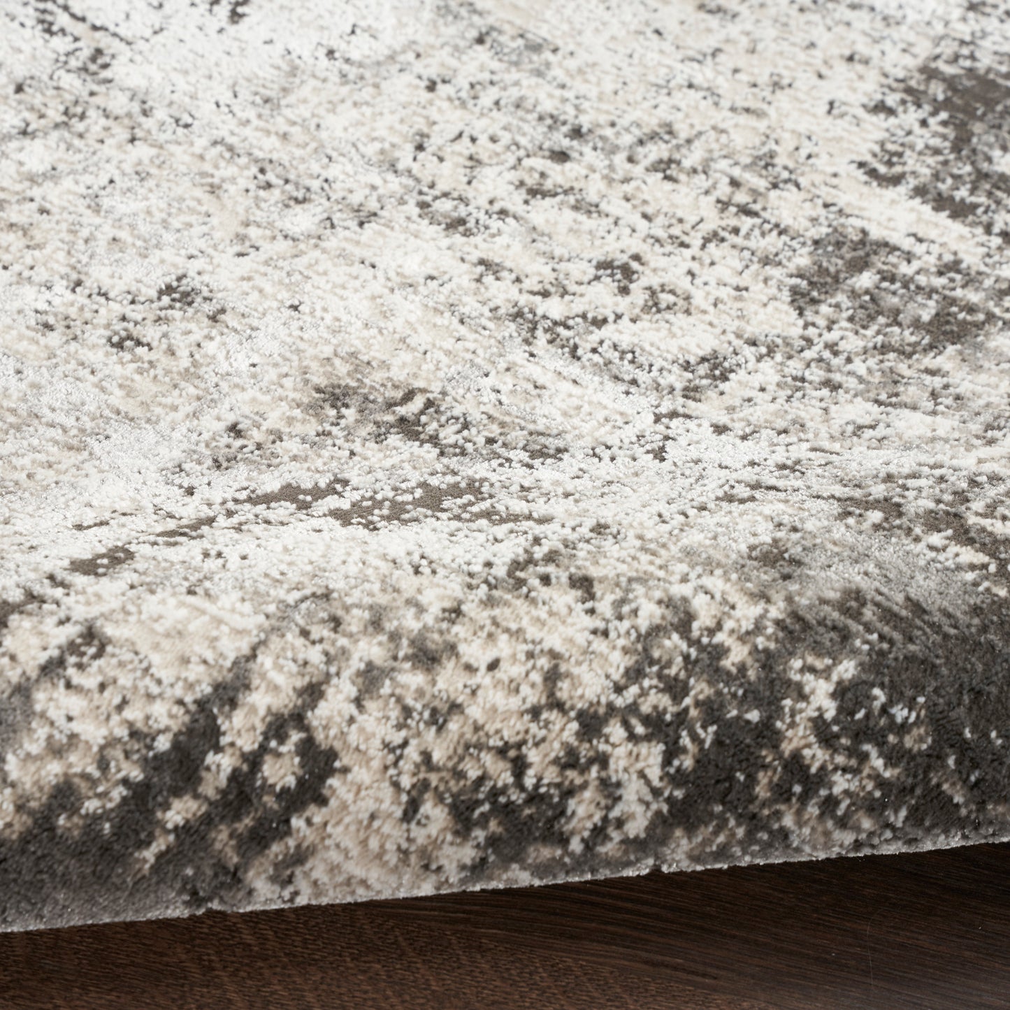 Plush gray-beige shag rug with an abstract speckled pattern, edge visible on dark wood floor.