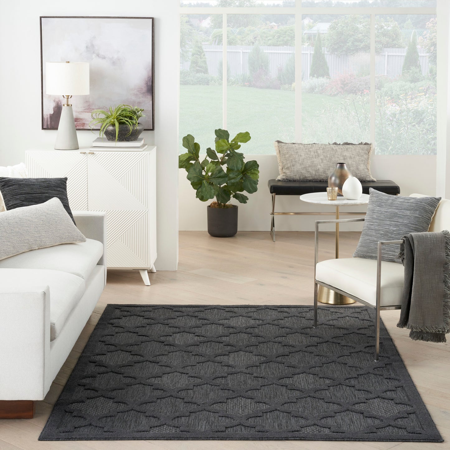 Charcoal geometric-pattern area rug in a bright contemporary living room with a white sofa and round glass coffee table.