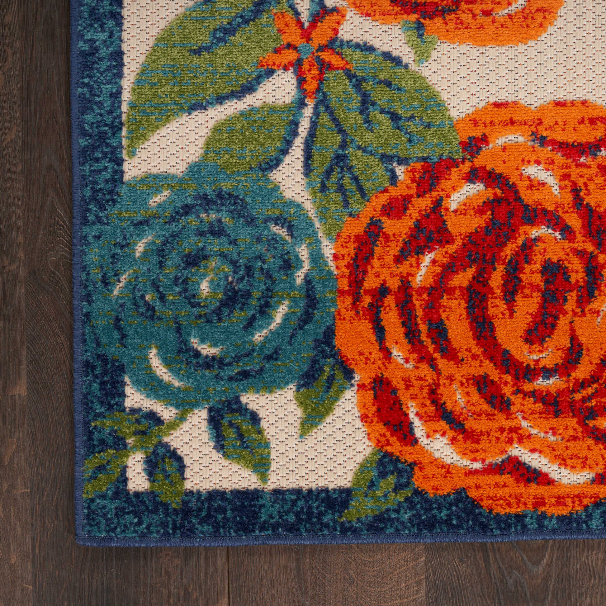 Woven floral rug with bright orange roses, teal-blue bloom, green leaves, beige background, dark blue border.