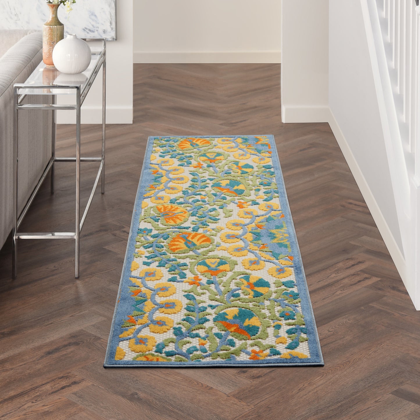 Long hallway runner rug with blue border and bright yellow, teal, and orange floral pattern on herringbone wood floor.