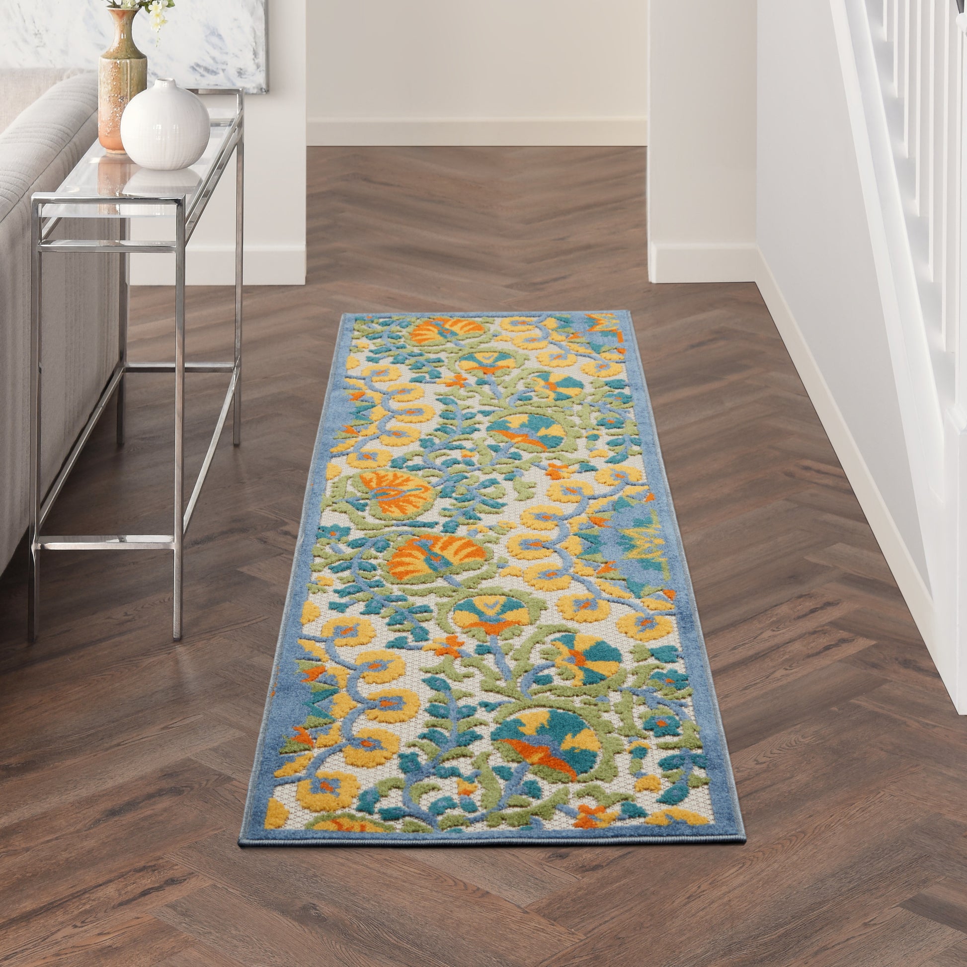 Long hallway runner rug with blue border and bright yellow, teal, and orange floral pattern on herringbone wood floor.