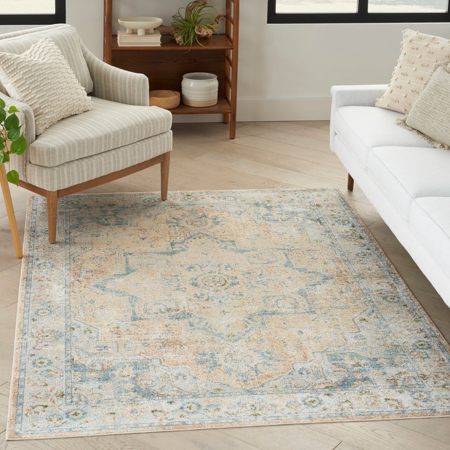 Distressed blue and cream oriental area rug in a bright living room with beige striped armchair and white sofa.