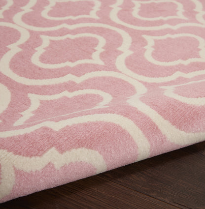 Pink plush rug with a white arabesque pattern on dark wood floor; soft pile with a folded corner.