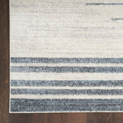 Beige area rug with dark blue stripes along the bottom edge on a dark wood floor.