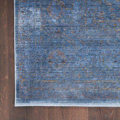 Blue distressed patterned area rug with faded gold and brown motifs, fringed edge, rectangular on dark wood floor.