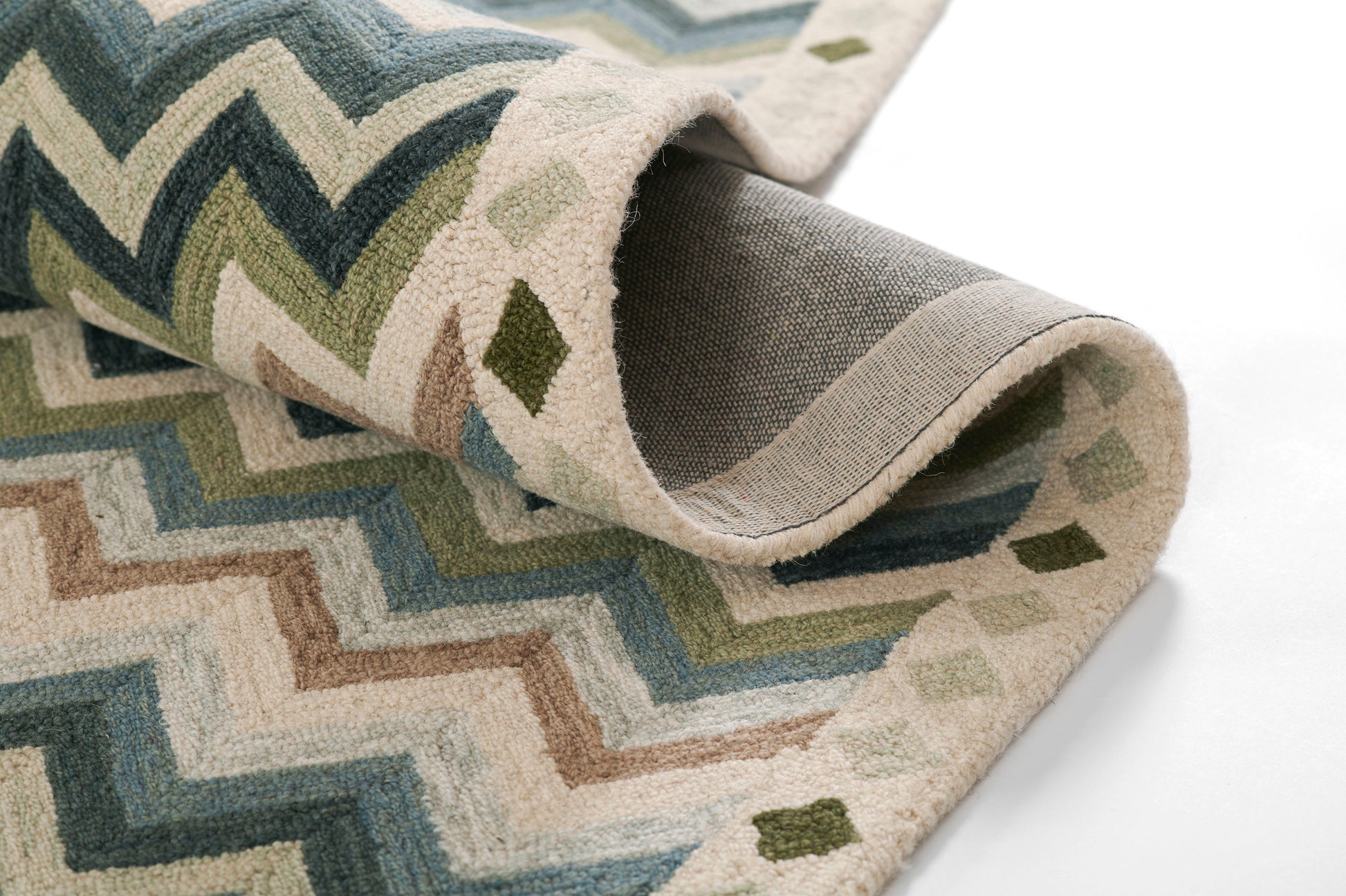 Chevron-pattern rug in blues, greens, and beige, folded to show plush woven texture.