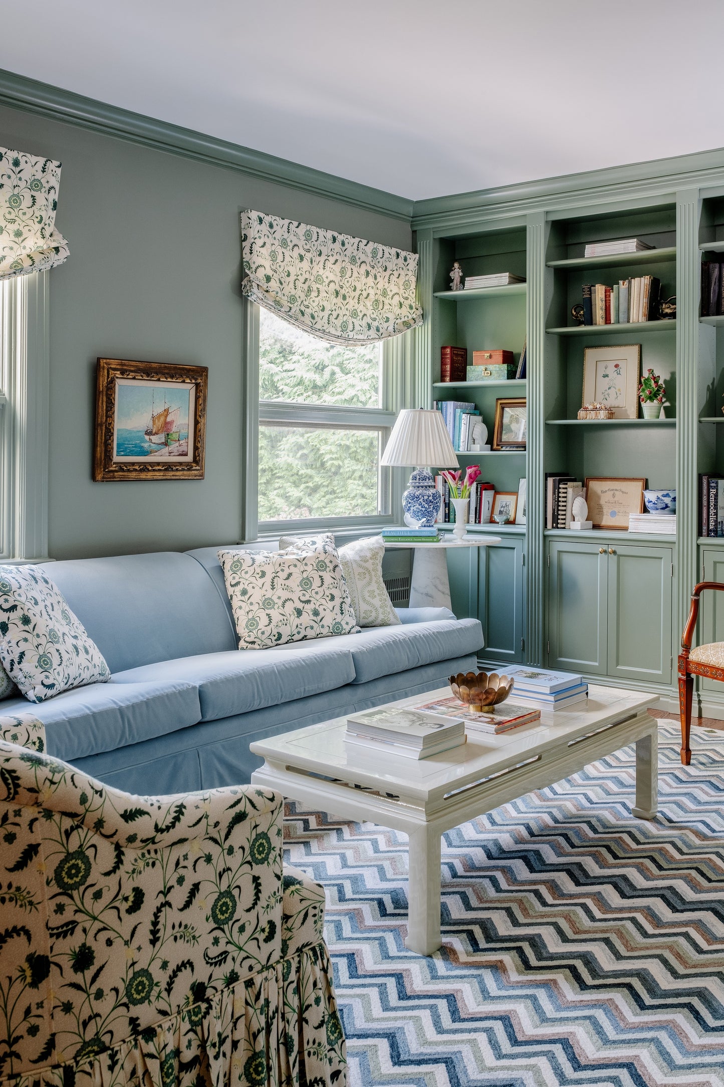 Cozy living room with pale blue sofa, floral cushions, mint-green built-in shelves, white coffee table, chevron rug.