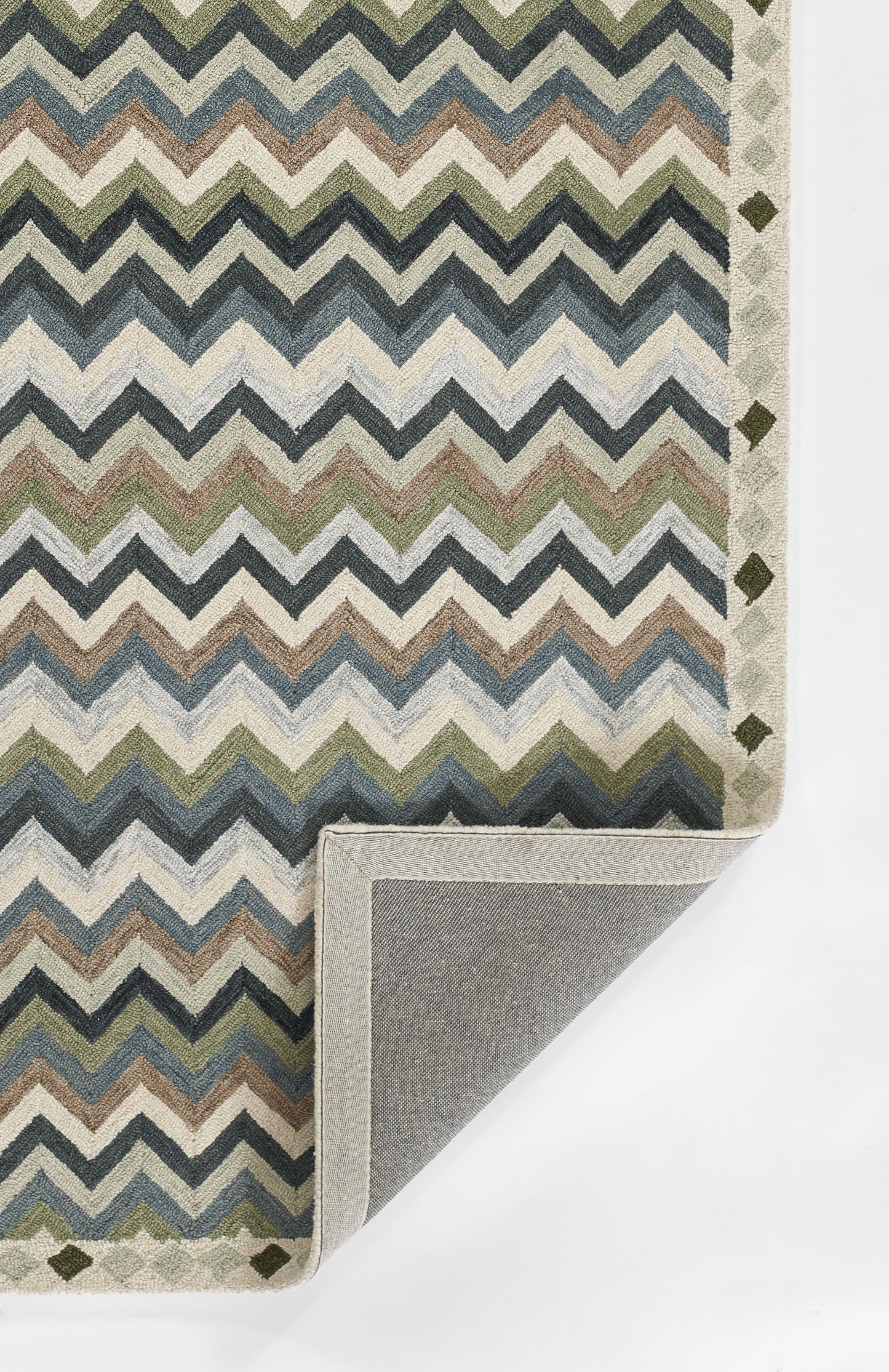 Chevron pattern rug in blues, greens & beiges; folded corner shows gray backing; border features small diamond shapes.