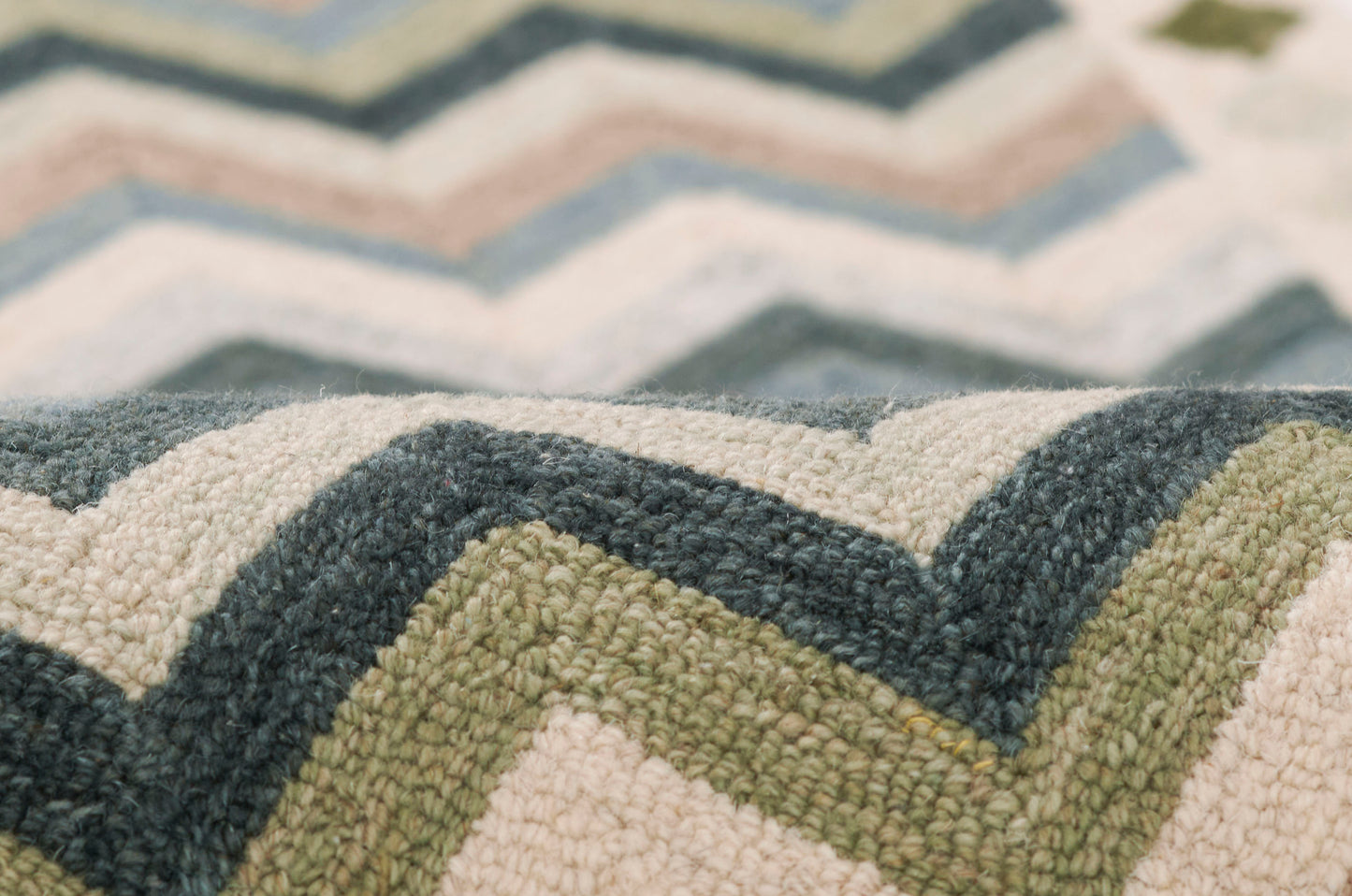 Close-up of a textured chevron rug in cream, blue-gray, and olive green with a boucle weave.