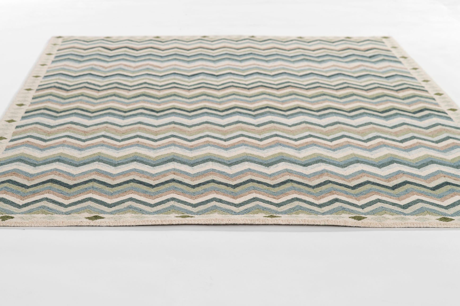 Rectangular flat-weave rug with blue-teal chevron zigzags, beige border and fringe.