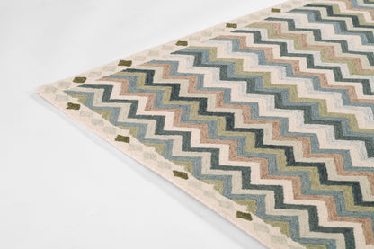 Chevron-pattern rug in blues, greens, and creams with beige border; flat-woven textile for living room decor.