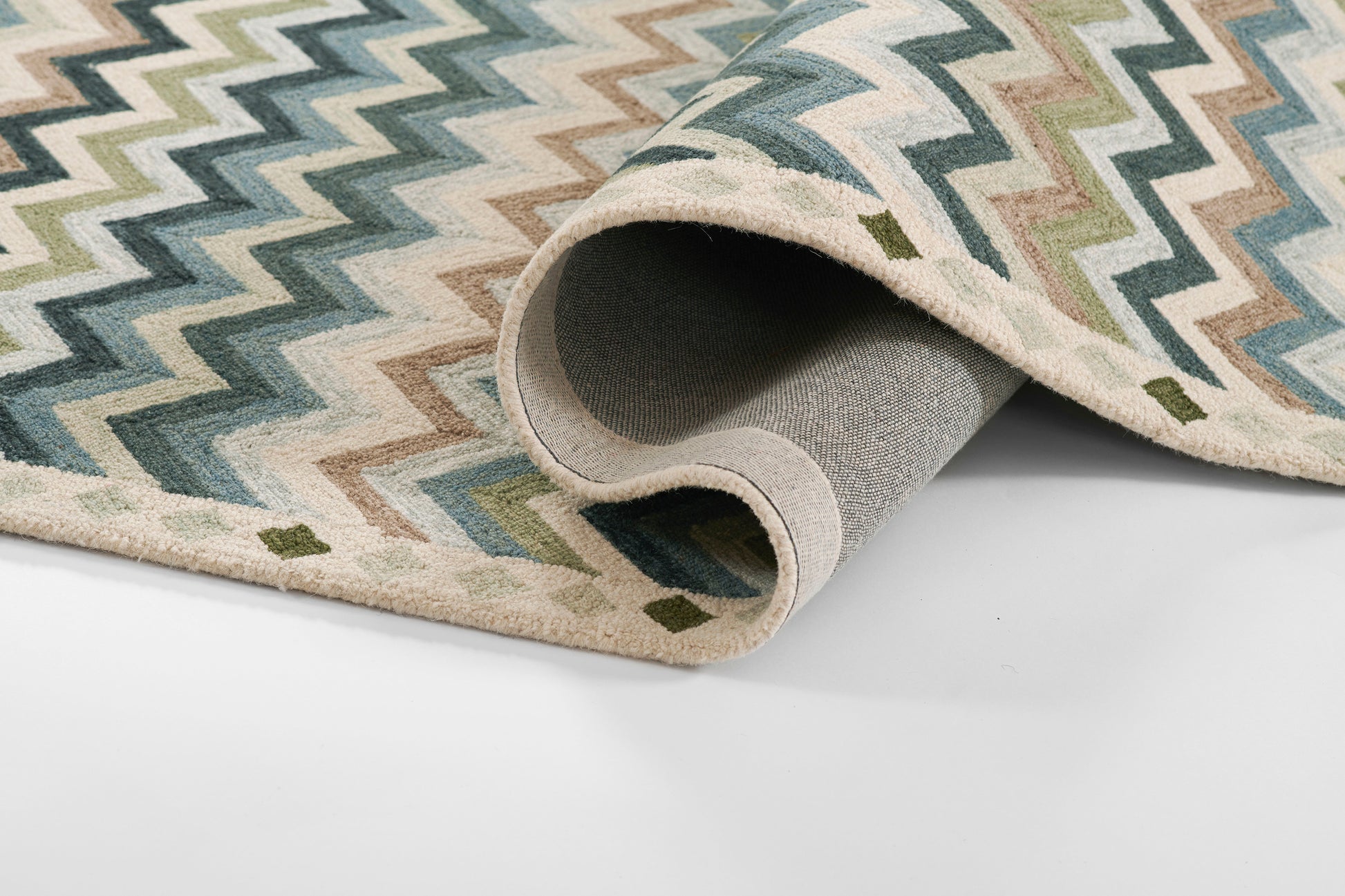 Chevron rug in blue, green & beige tones with cream border; woven flat-weave, rolled edge shows grey underside.