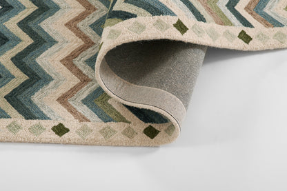 Chevron-pattern area rug in blues, teals, and beiges; folded edge reveals gray underside, modern geometric style.
