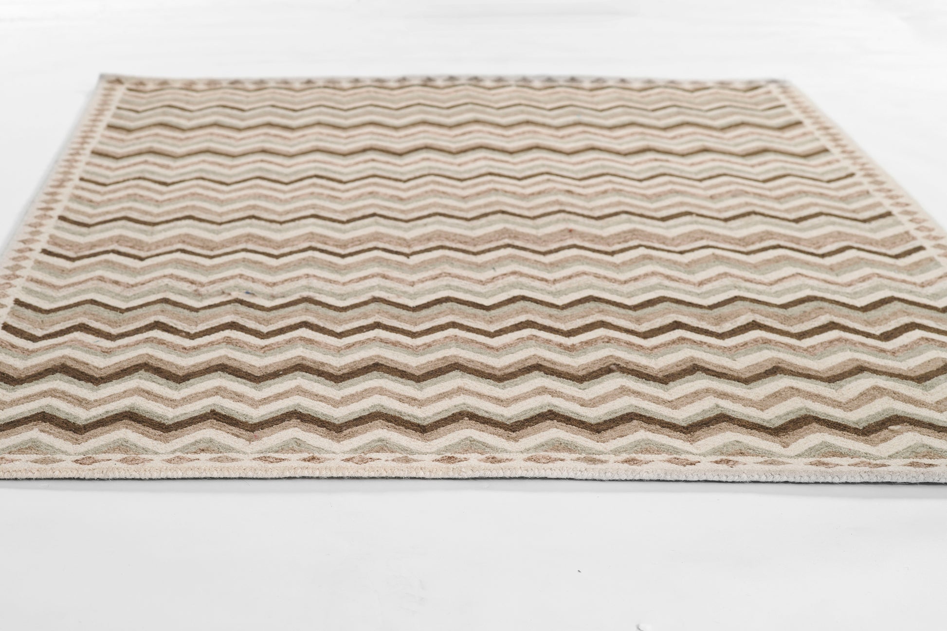 Rectangular woven rug with cream, beige and brown chevron pattern and fringed edges.