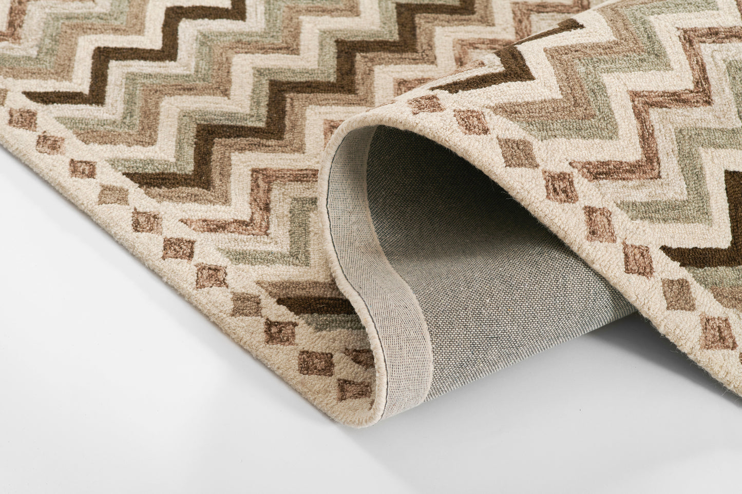 Beige chevron-pattern rug in tan, brown and cream; rolled edge shows grey backing