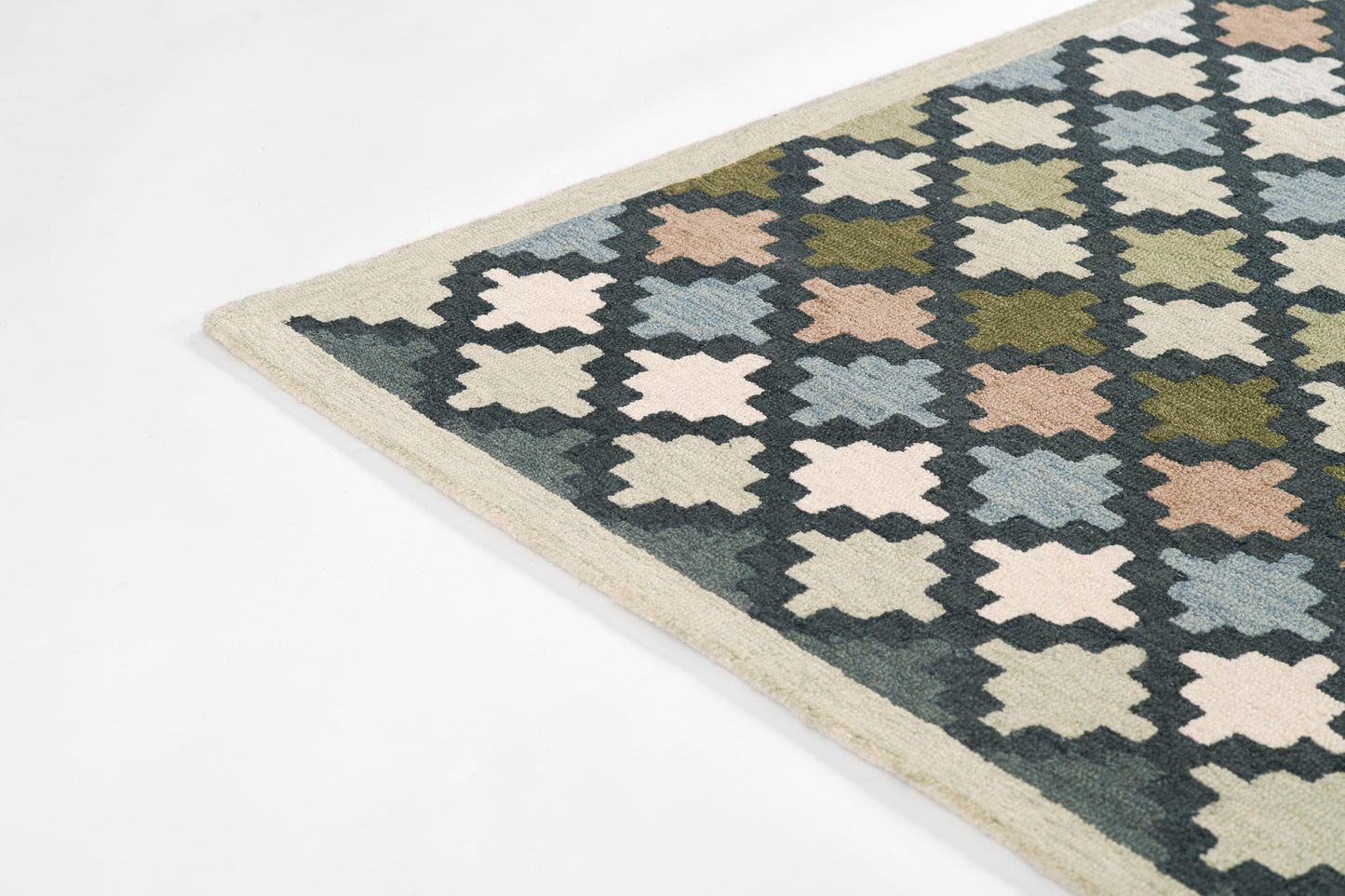 Rectangular flatwoven rug with repeating cross/star geometric motif in navy, cream, olive, pale pink and light blue, beige border.