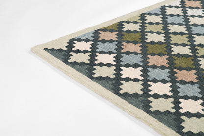 Rectangular flatwoven rug with repeating cross/star geometric motif in navy, cream, olive, pale pink and light blue, beige border.