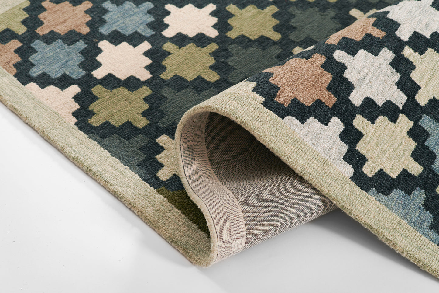 Geometric diamond trellis rug in navy, beige, peach and olive; flat-weave with rolled edge and light tan backing.