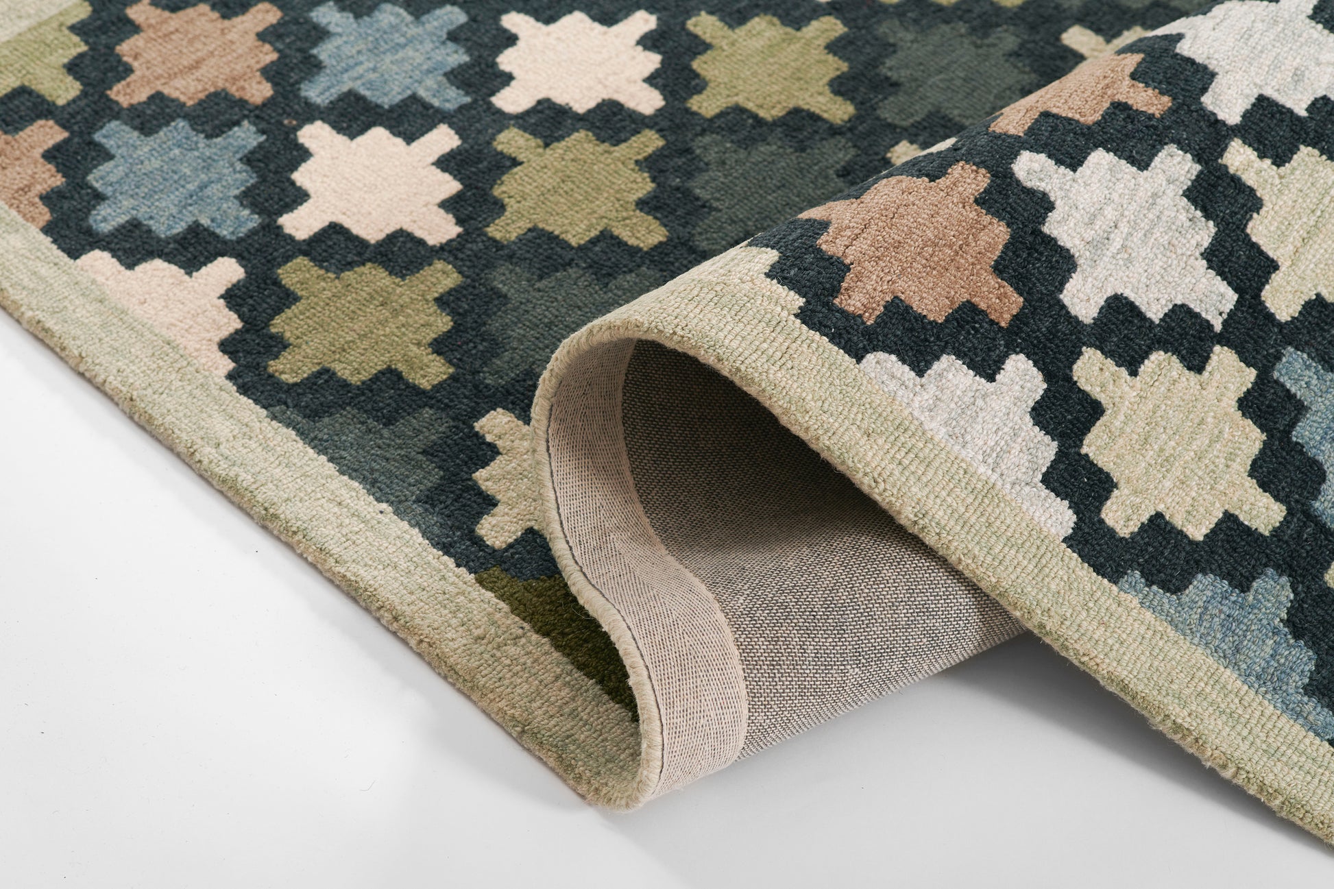 Geometric diamond trellis rug in navy, beige, peach and olive; flat-weave with rolled edge and light tan backing.