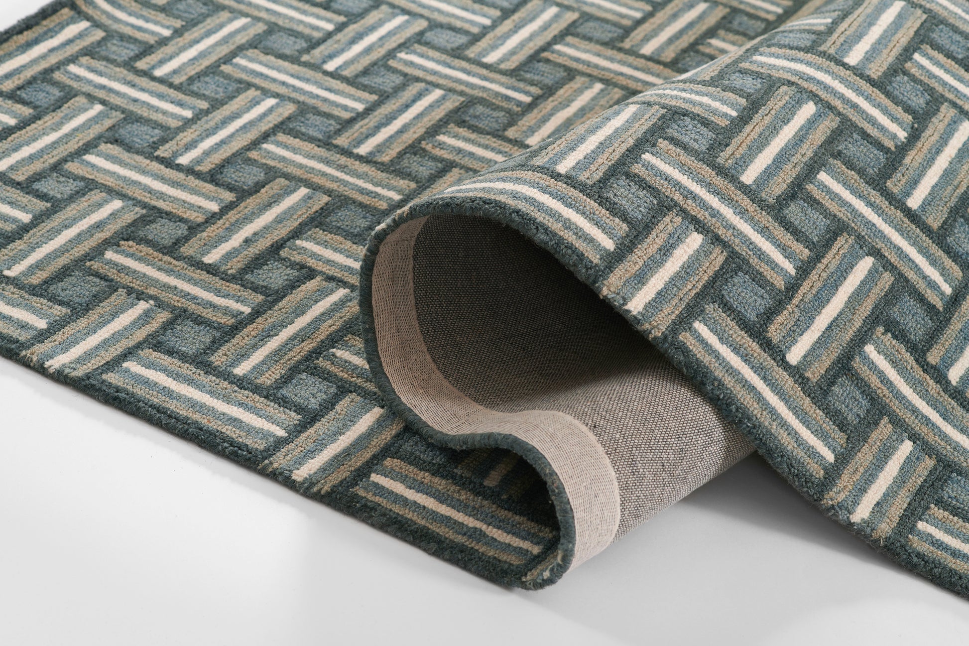 Geometric woven rug in teal, blue and beige with lattice pattern; rolled edge reveals soft backing, ideal area rug.