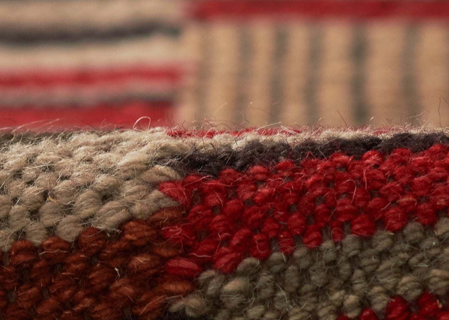 Macro shot of a textured wool rug with red, beige, gray and brown woven stripes.