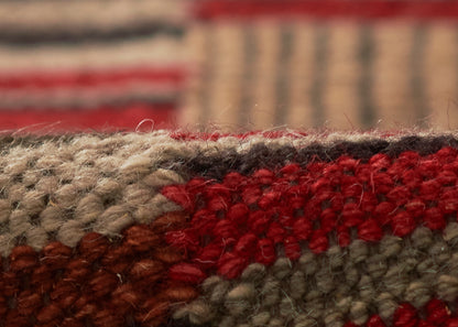 Macro shot of a textured wool rug with red, beige, gray and brown woven stripes.