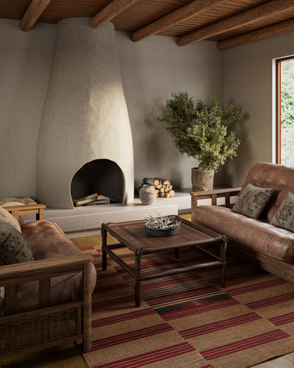 Adobe-style living room with a tall curved fireplace, wood-beamed ceiling, brown leather sofas, wooden coffee table, striped rug.