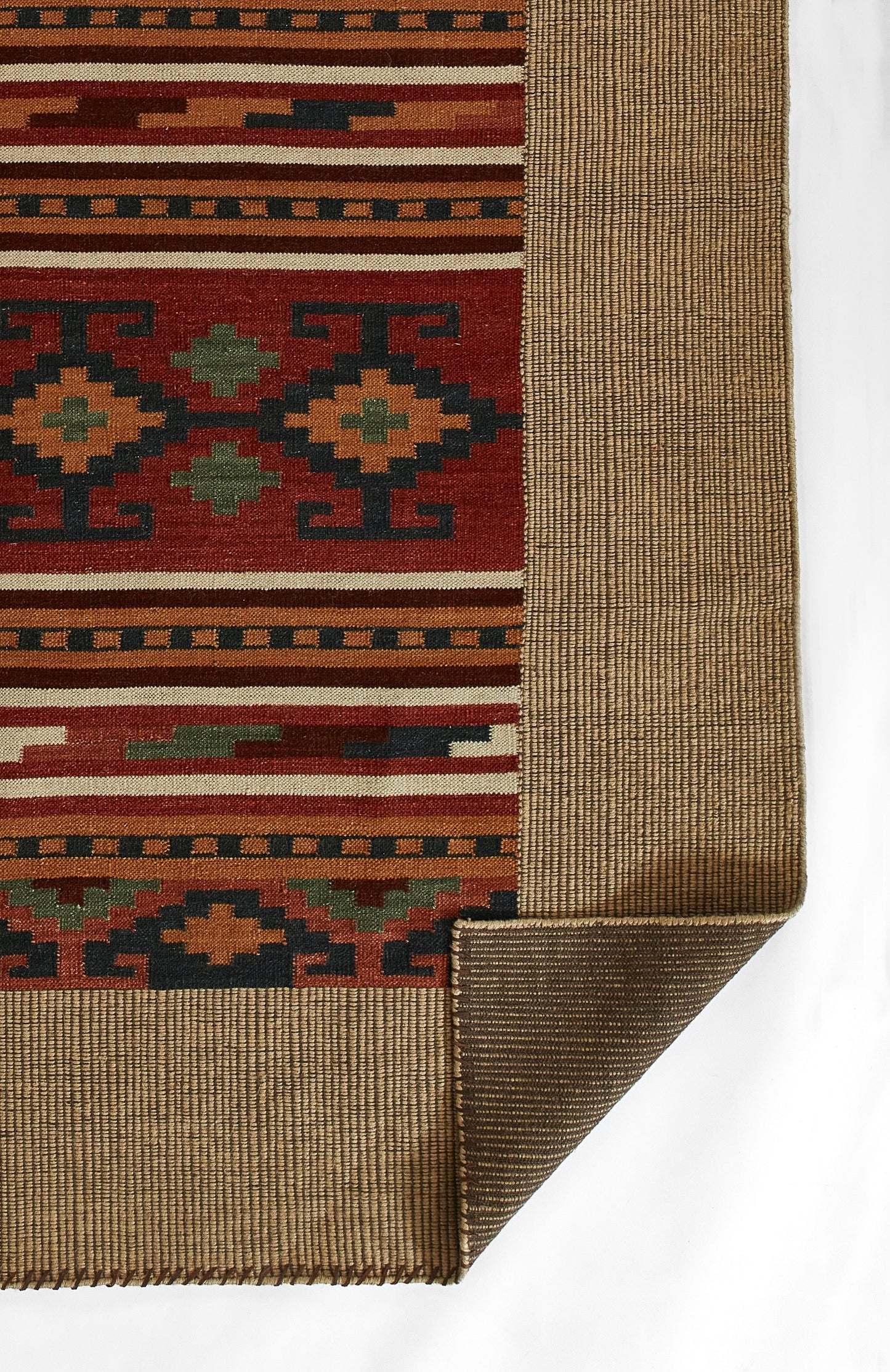 Woven rug with red field and geometric Aztec motifs in green, yellow, blue; beige border; folded corner.