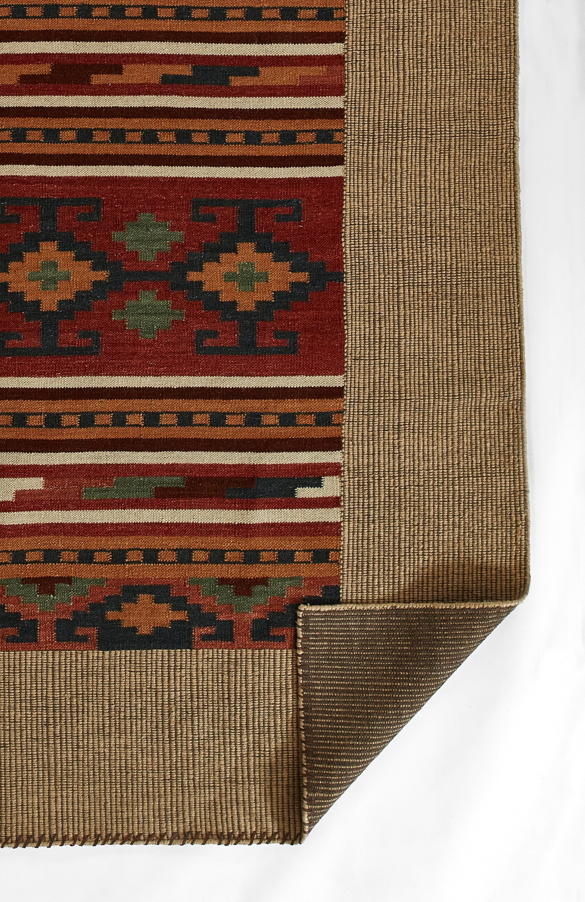 Woven rug with red field and geometric Aztec motifs in green, yellow, blue; beige border; folded corner.