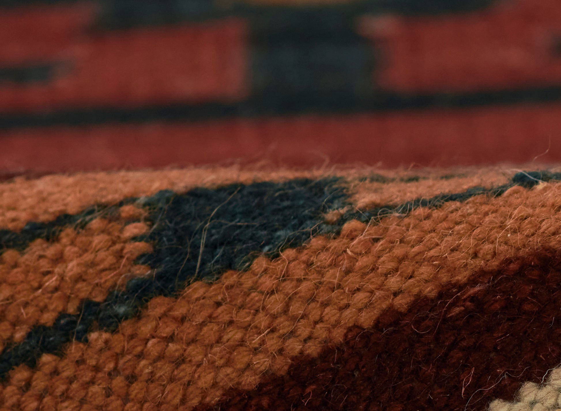 Close-up of a chunky-woven wool rug in orange, black and brown geometric pattern.