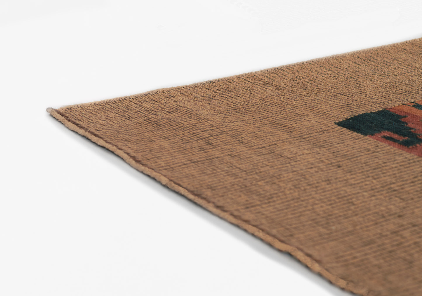 Brown woven rug corner with textured natural fiber and a small black-red geometric motif.