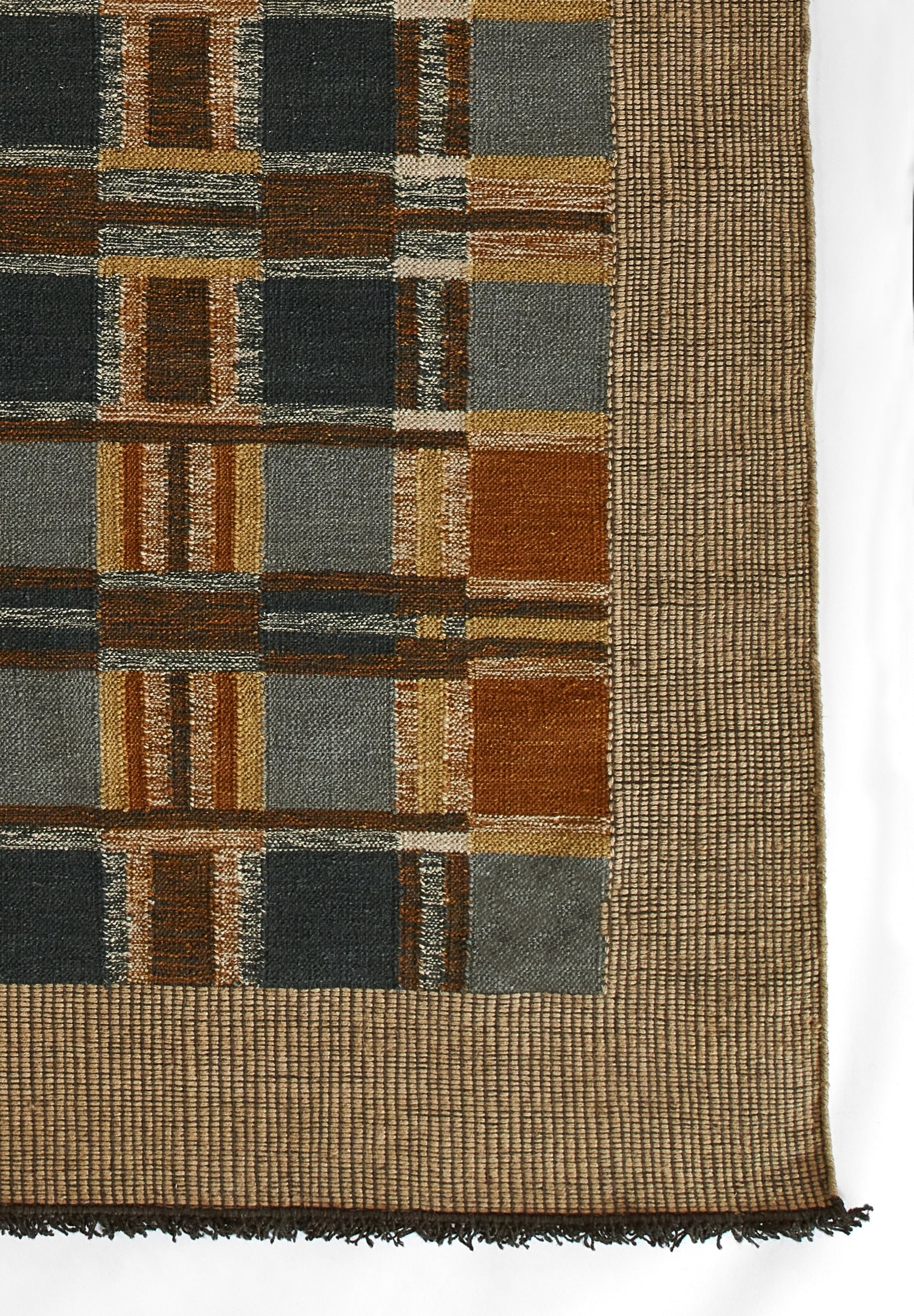 Woven rug with brown, tan, gray and blue blocks in a geometric plaid pattern, bordered by a tan weave and fringed edge.