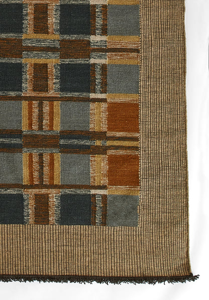 Geometric woven rug with blue, brown, gray and gold rectangular blocks in a grid, tan border and fringe.
