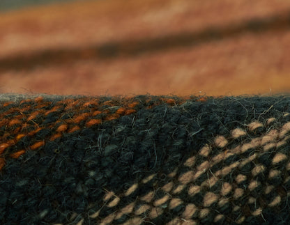 Close-up of a woven plaid textile in dark blue, burnt orange, and beige; fuzzy wool blend, cozy scarf or throw.