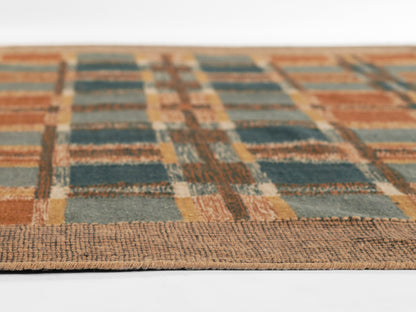 Woven plaid rug in orange, teal and brown with textured border fringe; low-angle close-up.