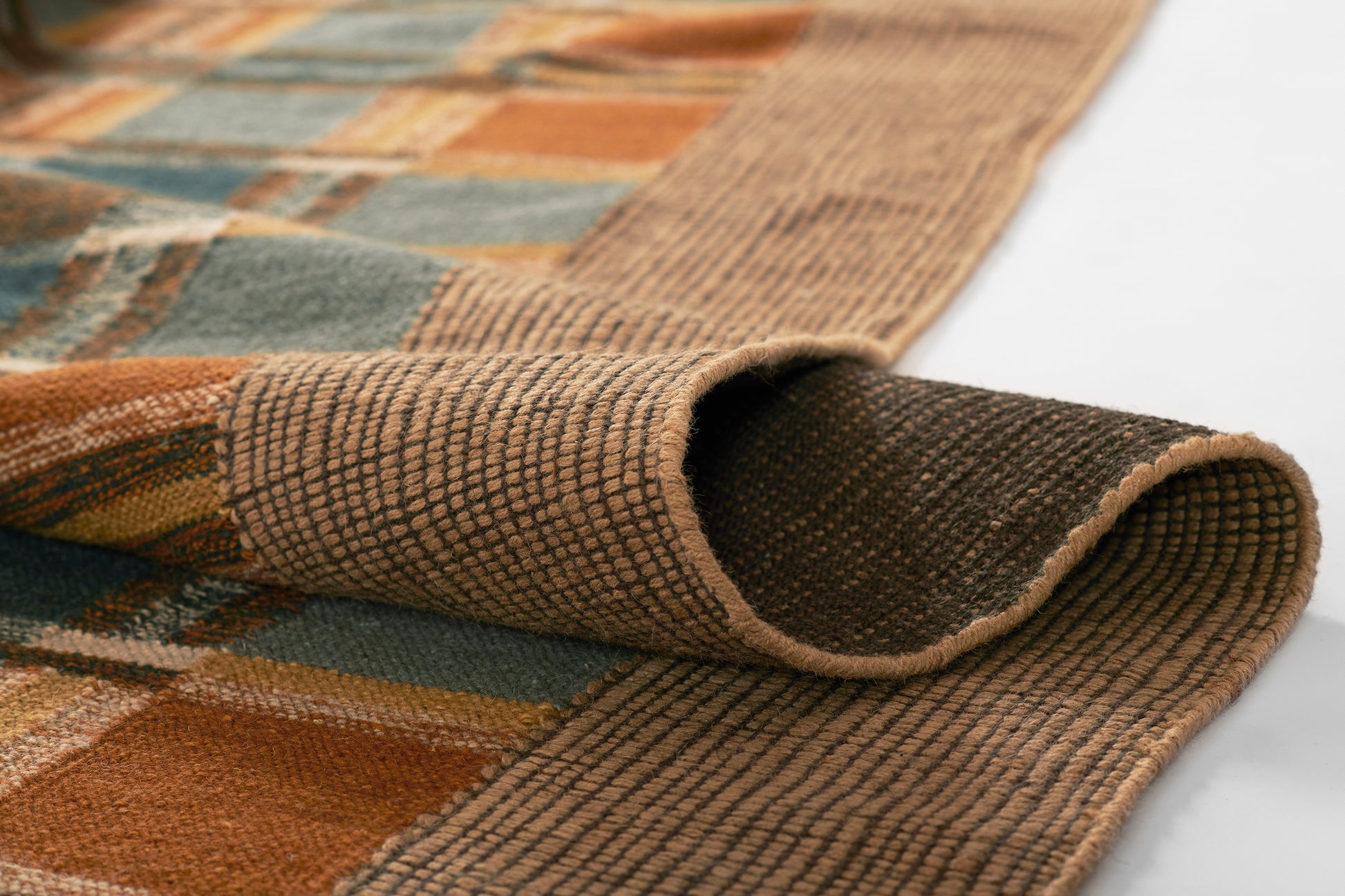 Rust orange, teal, and beige plaid woven rug with brown backing; folded corner shows textured weave.