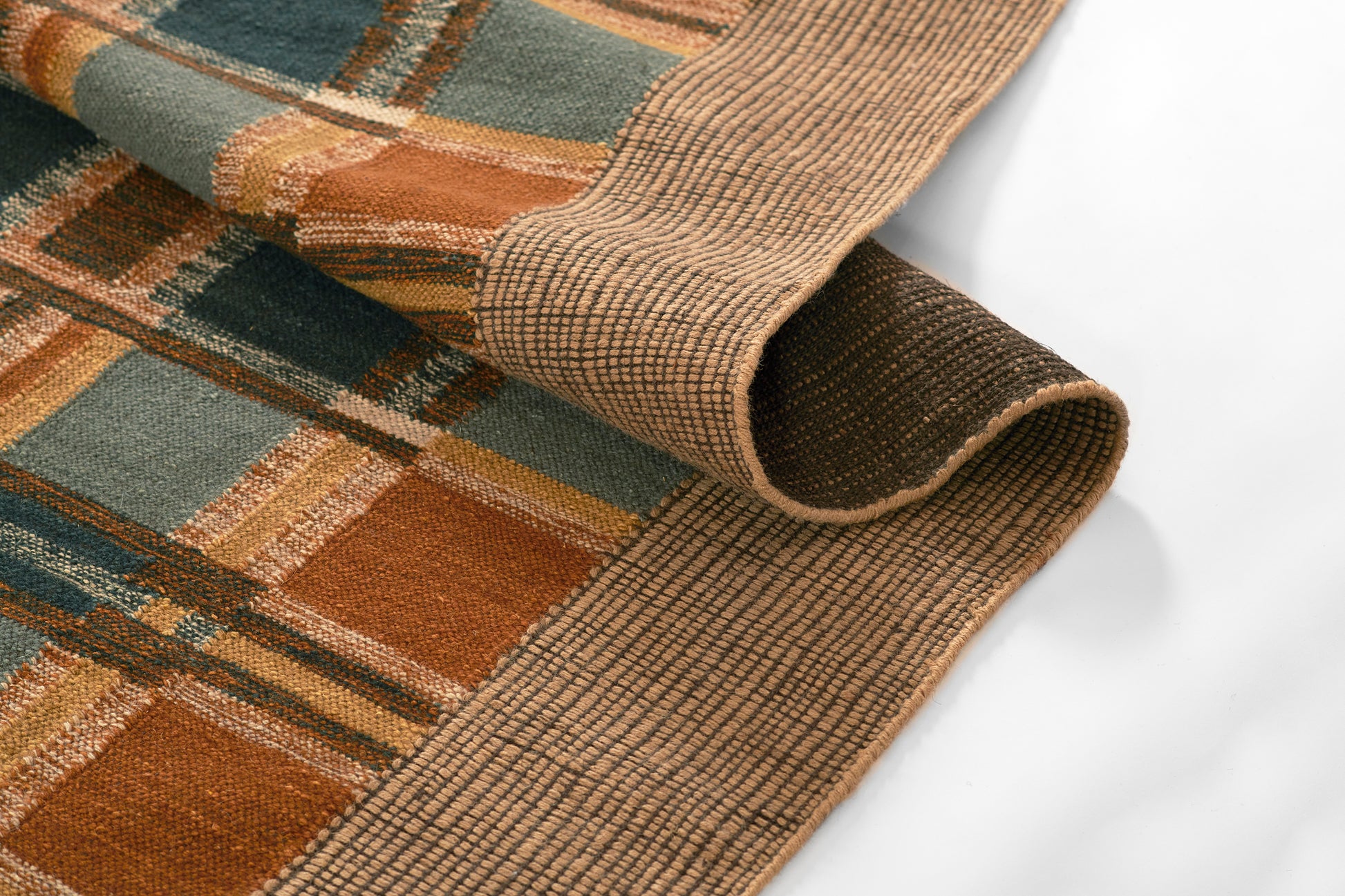 Woven plaid textile rug with orange, teal, grey blocks and beige border; rolled edge.