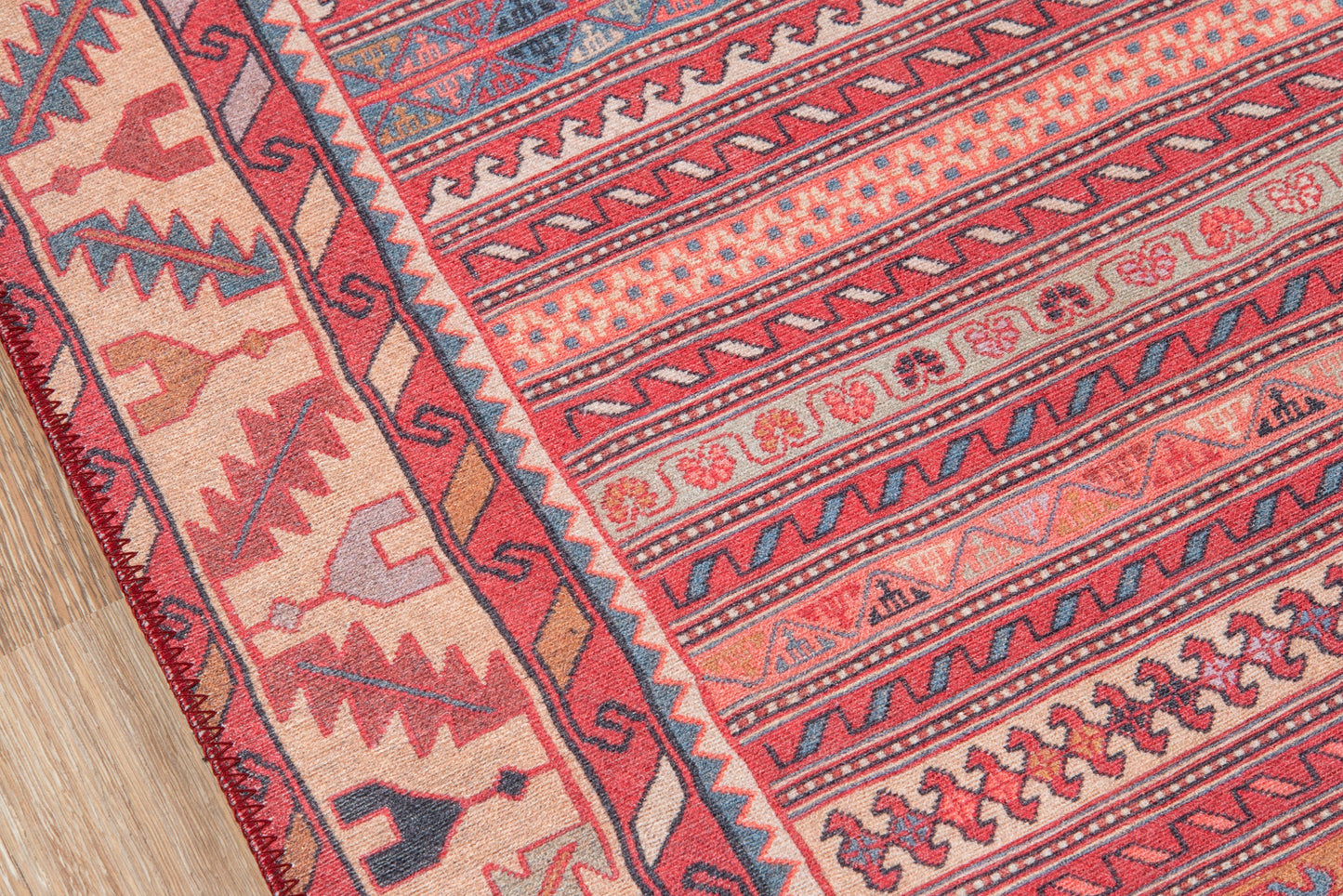 Colorful geometric kilim rug with red, pink, and blue tribal motifs and border fringe on wood floor.