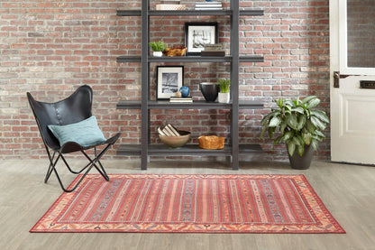 Boho living room: red patterned rug, black metal shelving, butterfly chair with turquoise cushion, brick wall, potted plant.