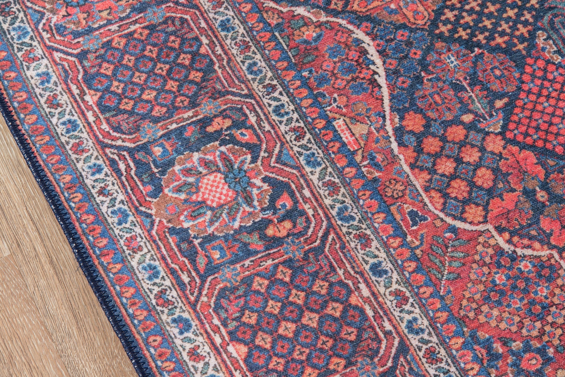 Persian-style rug with navy, red, and cream floral motifs, ornate border, fringe edge on a wooden floor.
