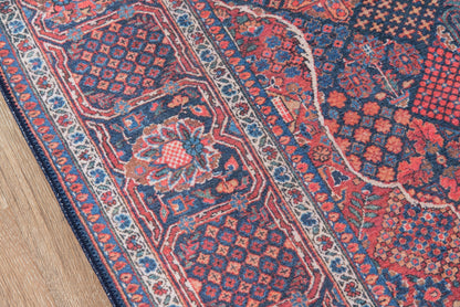 Persian-style oriental rug in navy, red, and ivory with geometric floral motifs and decorative borders on a wooden floor